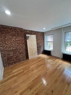 unfurnished living room with brick wall and light hardwood / wood-style flooring