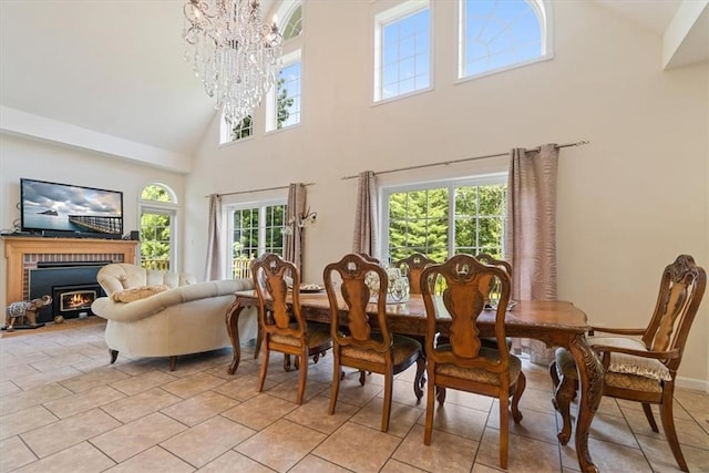 tiled dining area with a brick fireplace, a wealth of natural light, a high ceiling, and an inviting chandelier