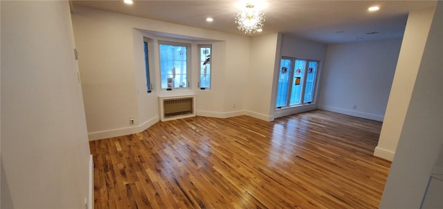 empty room featuring hardwood / wood-style floors, an inviting chandelier, and radiator heating unit