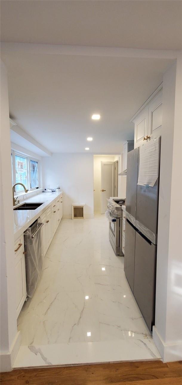 kitchen with stainless steel appliances, white cabinetry, light hardwood / wood-style floors, and sink