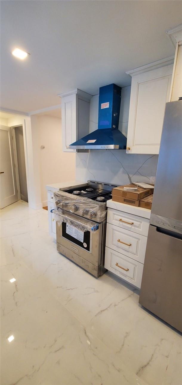 kitchen featuring decorative backsplash, appliances with stainless steel finishes, white cabinetry, and wall chimney range hood