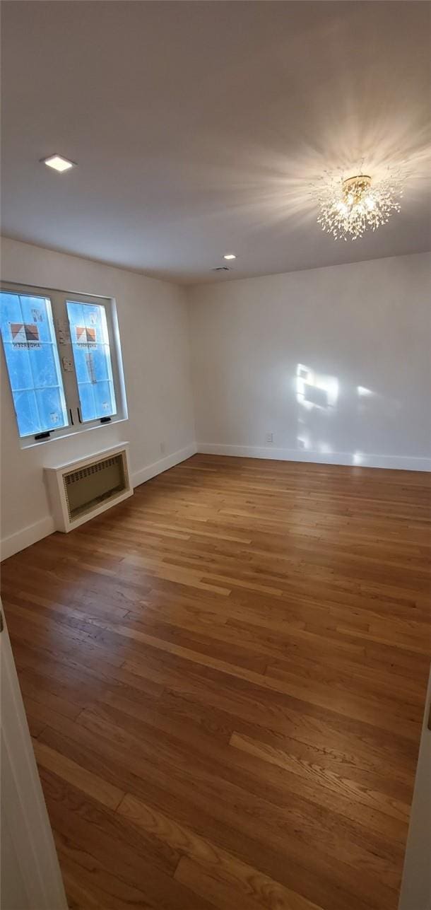 spare room with hardwood / wood-style flooring, an inviting chandelier, and an AC wall unit