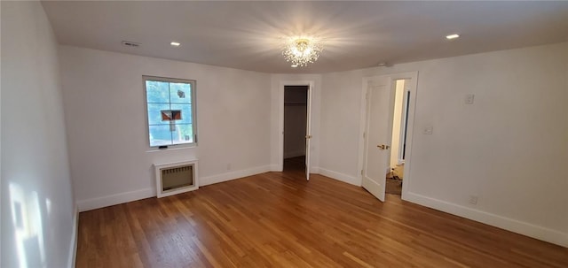 empty room with heating unit, a chandelier, and hardwood / wood-style flooring