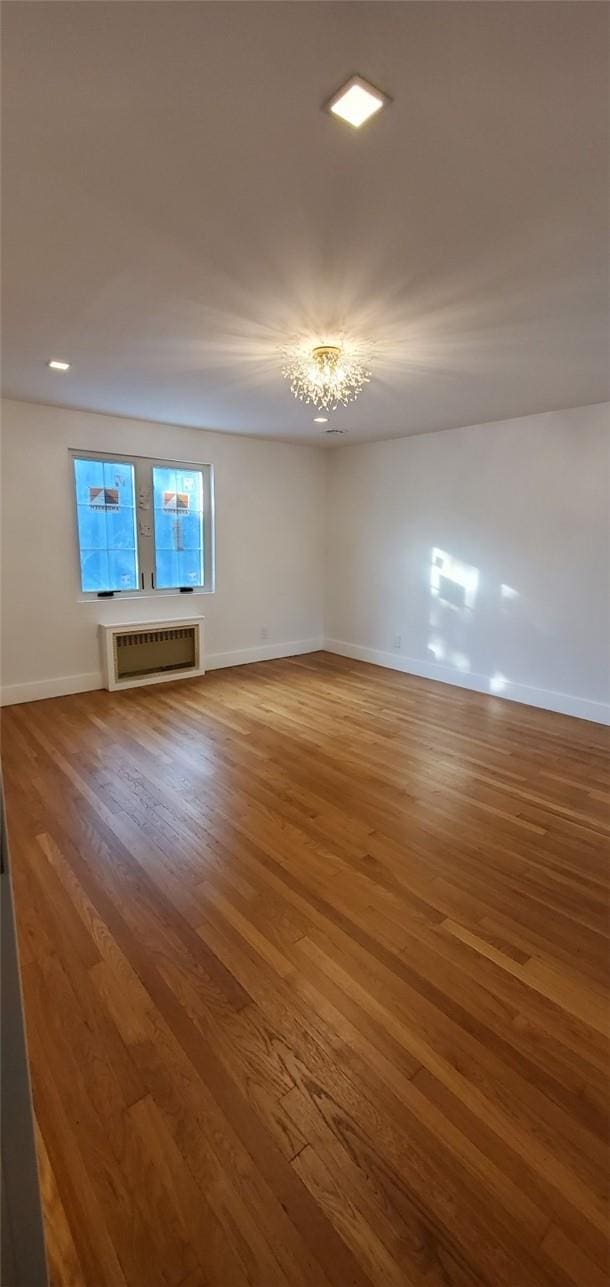 empty room featuring a chandelier, hardwood / wood-style floors, and an AC wall unit