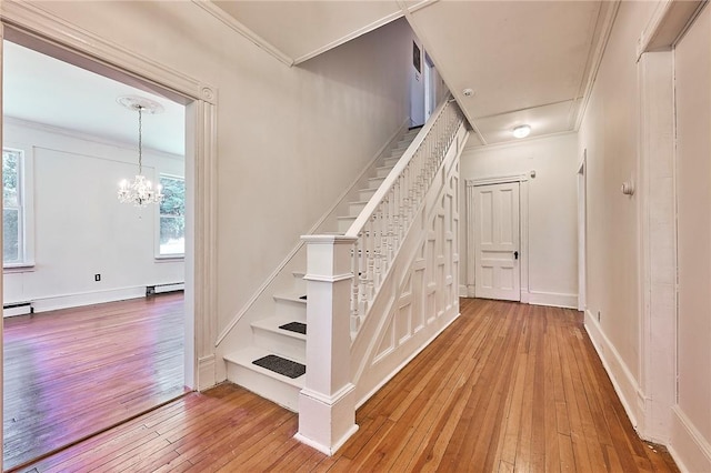 stairs with crown molding, wood-type flooring, and an inviting chandelier