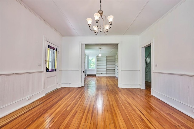 unfurnished dining area with an inviting chandelier, ornamental molding, and light wood-type flooring