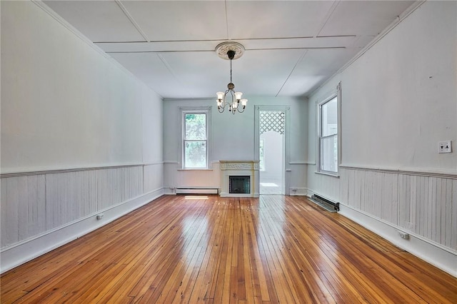 unfurnished living room featuring baseboard heating, a chandelier, and hardwood / wood-style flooring