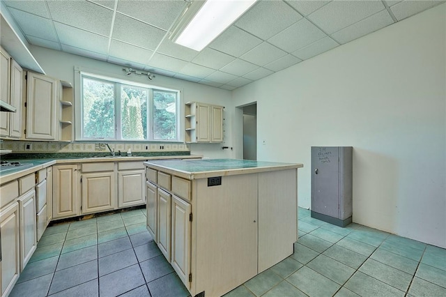 kitchen with stovetop, sink, a center island, light tile patterned floors, and a drop ceiling