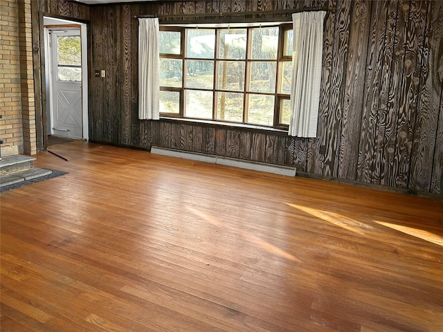 empty room with wood-type flooring, brick wall, a baseboard heating unit, and wooden walls