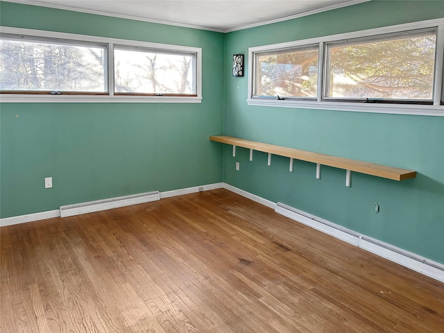 empty room featuring baseboard heating, ornamental molding, and wood-type flooring