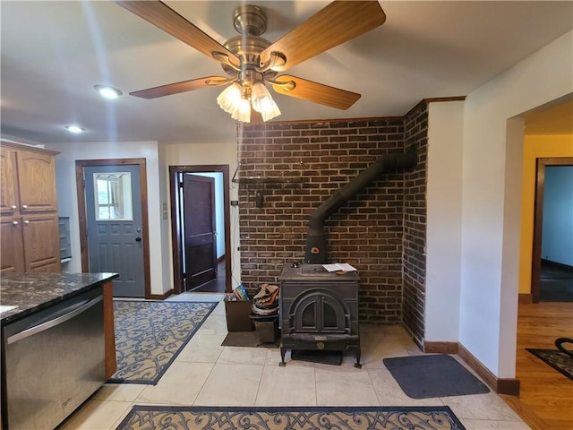 interior space with a wood stove, ceiling fan, dishwasher, light hardwood / wood-style flooring, and dark stone counters