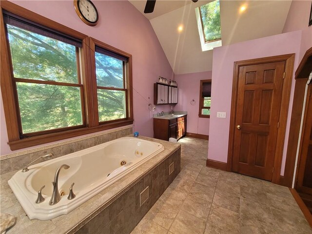 bathroom with vanity, tile patterned floors, tiled tub, and vaulted ceiling with skylight