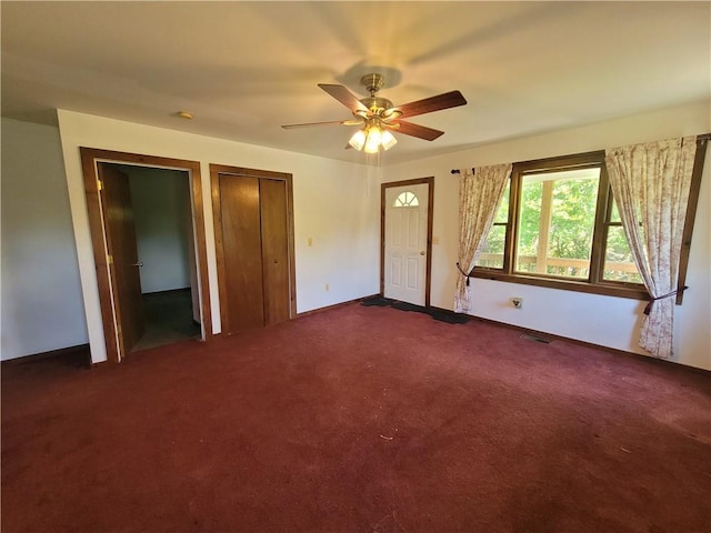 unfurnished bedroom with two closets, dark carpet, and ceiling fan