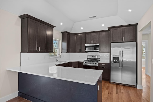 kitchen featuring sink, appliances with stainless steel finishes, dark brown cabinets, decorative backsplash, and kitchen peninsula