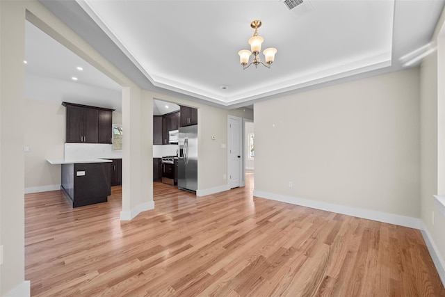 unfurnished living room featuring a raised ceiling, a chandelier, and light wood-type flooring