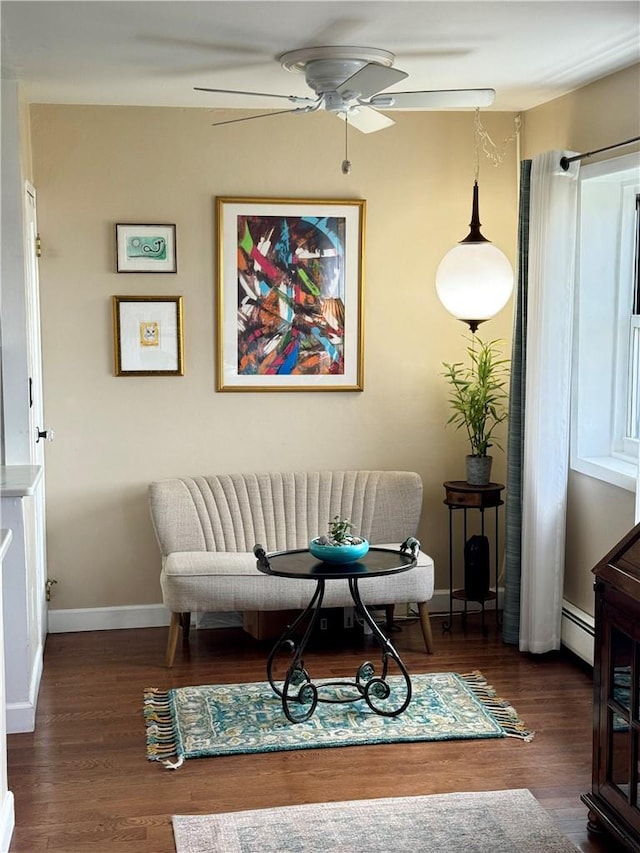 living area featuring dark hardwood / wood-style floors, ceiling fan, and a baseboard heating unit