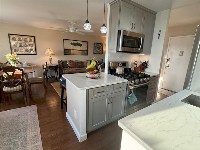 kitchen with gray cabinetry, dark wood-type flooring, decorative light fixtures, decorative backsplash, and appliances with stainless steel finishes