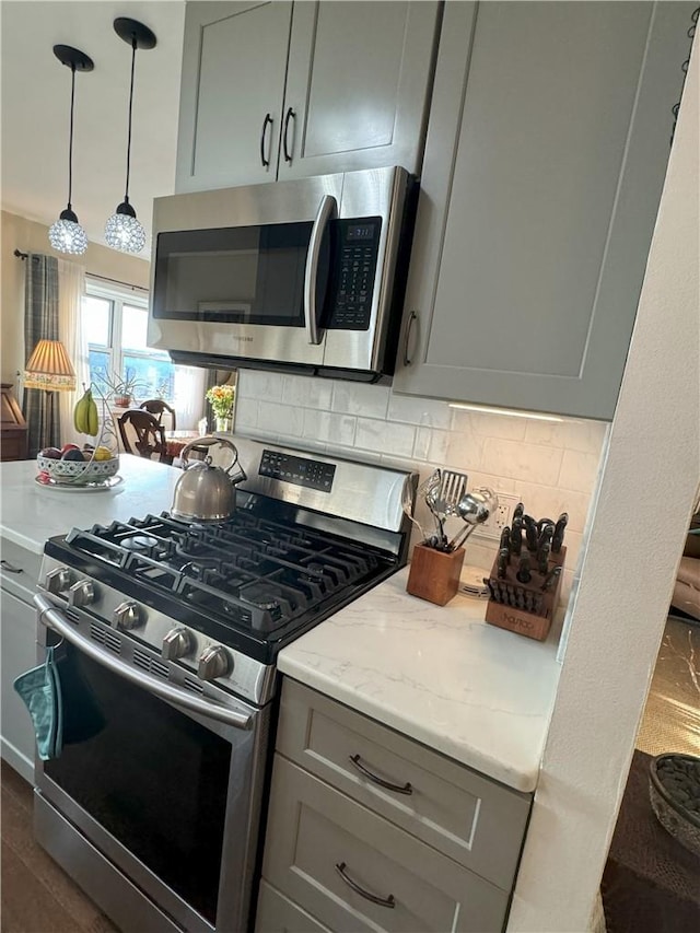 kitchen featuring backsplash, gray cabinetry, light stone countertops, and appliances with stainless steel finishes