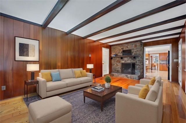 living room featuring wooden walls, a fireplace, beamed ceiling, and light hardwood / wood-style floors