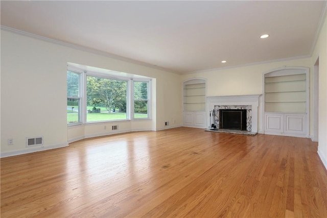 unfurnished living room with light hardwood / wood-style floors, built in features, ornamental molding, and a premium fireplace