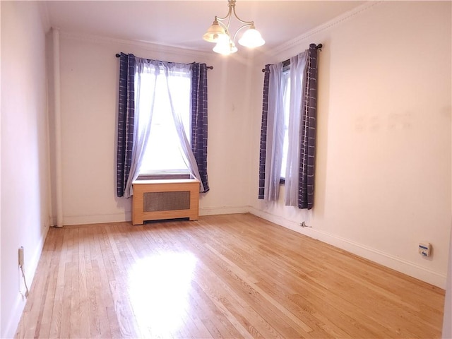 empty room featuring hardwood / wood-style flooring, a notable chandelier, radiator heating unit, and ornamental molding