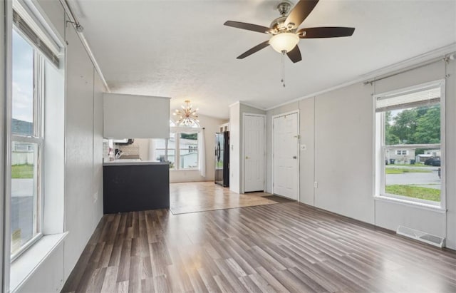 unfurnished living room with a textured ceiling, ornamental molding, ceiling fan with notable chandelier, and hardwood / wood-style flooring