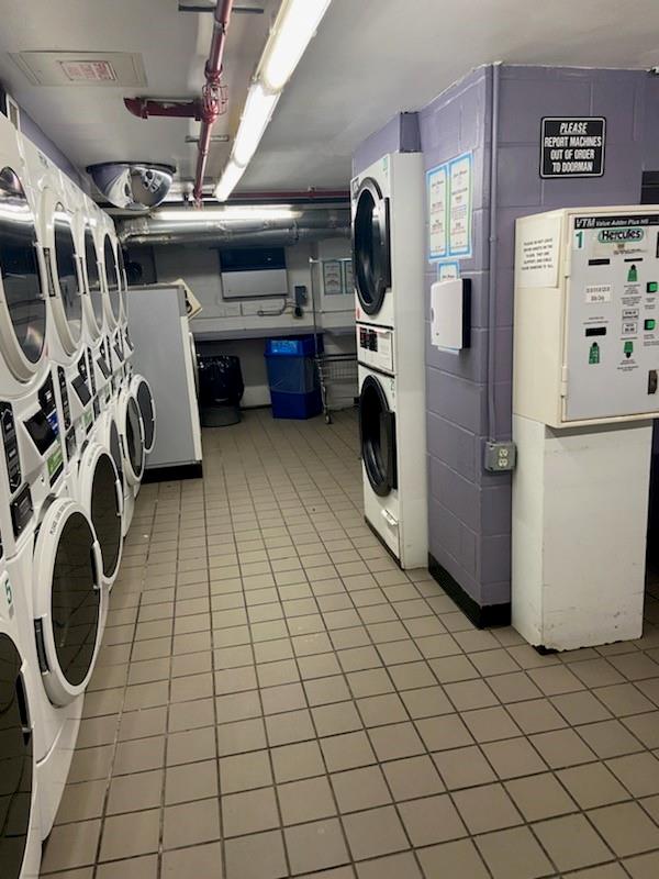 laundry area with stacked washing maching and dryer and light tile patterned floors