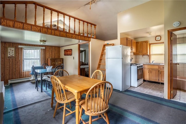 dining space featuring wood walls, sink, a high ceiling, and a baseboard heating unit