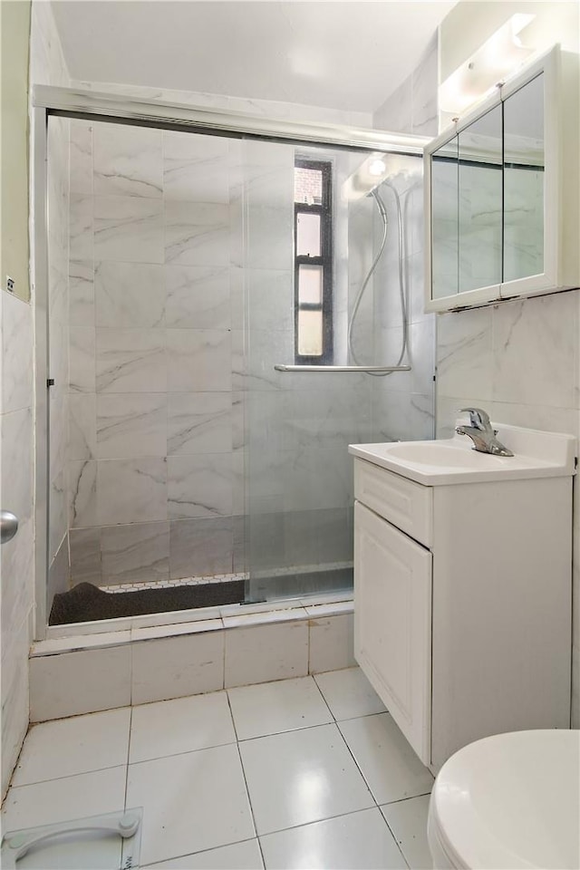 bathroom featuring tile patterned floors, a shower with door, vanity, and tile walls