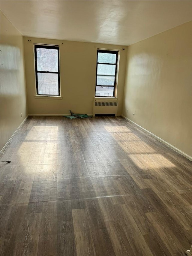 unfurnished room featuring hardwood / wood-style floors, a healthy amount of sunlight, and radiator heating unit