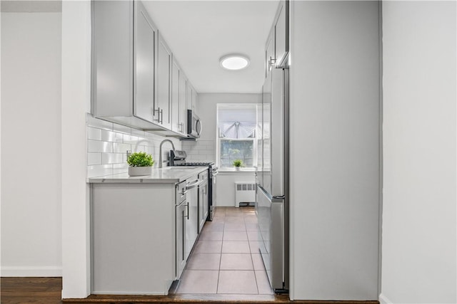 kitchen with tasteful backsplash, radiator heating unit, light tile patterned floors, and stainless steel appliances