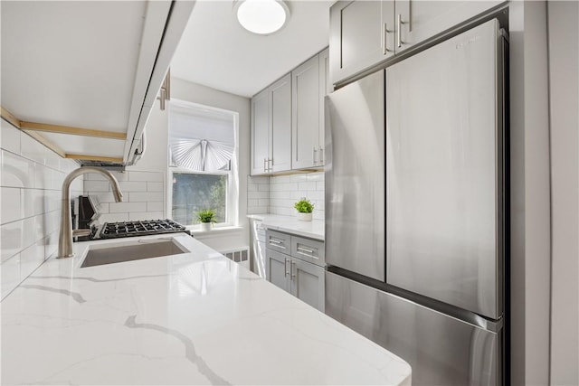 kitchen featuring light stone countertops, sink, tasteful backsplash, stainless steel fridge, and gray cabinets