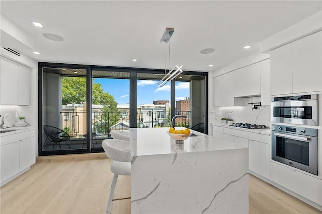 kitchen with a kitchen island with sink, a wall of windows, light hardwood / wood-style floors, white cabinetry, and hanging light fixtures