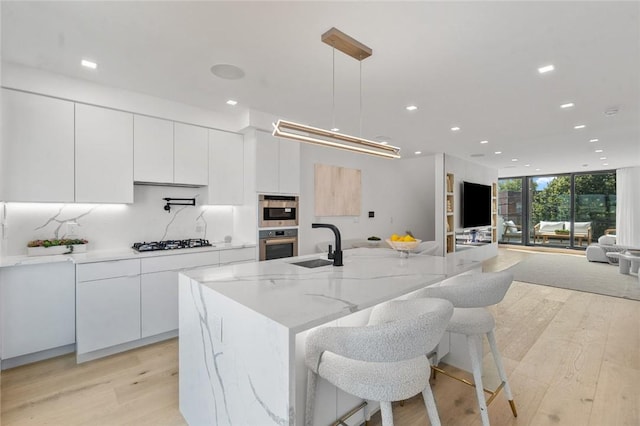 kitchen with hanging light fixtures, light hardwood / wood-style flooring, a spacious island, stainless steel gas stovetop, and white cabinets