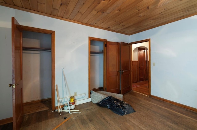 unfurnished bedroom with two closets, wooden ceiling, dark hardwood / wood-style floors, and ornamental molding