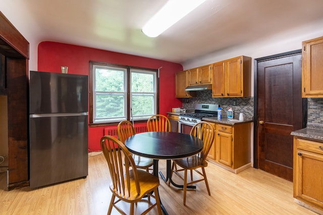 kitchen with tasteful backsplash, stainless steel gas range oven, black fridge, and light wood-type flooring