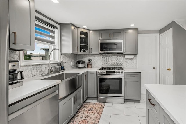 kitchen with gray cabinetry, sink, decorative backsplash, light tile patterned floors, and appliances with stainless steel finishes