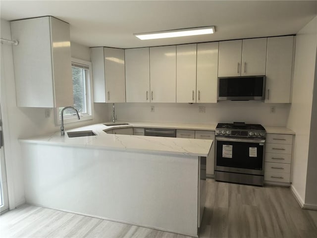 kitchen featuring kitchen peninsula, stainless steel appliances, light hardwood / wood-style flooring, and sink