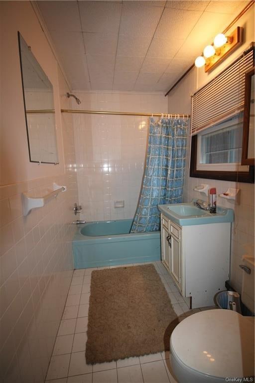 full bathroom featuring tile patterned floors, shower / bath combination with curtain, toilet, vanity, and tile walls