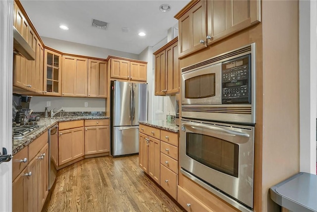 kitchen featuring light stone countertops, light wood-type flooring, stainless steel appliances, and sink