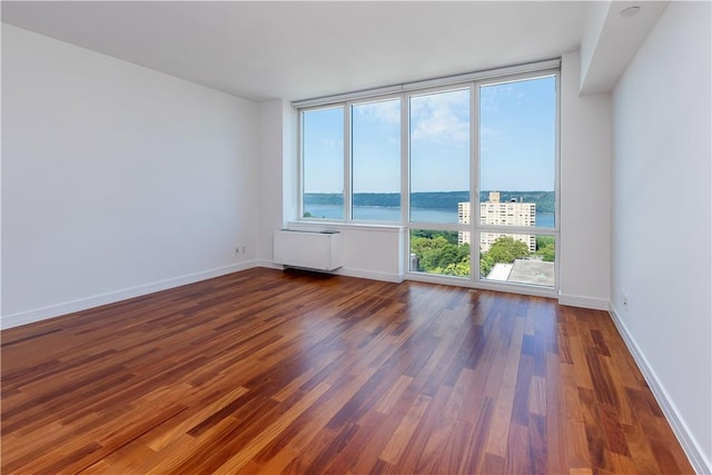 unfurnished room featuring radiator, a water view, and dark wood-type flooring