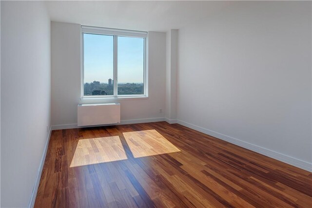 unfurnished room featuring hardwood / wood-style floors and radiator heating unit