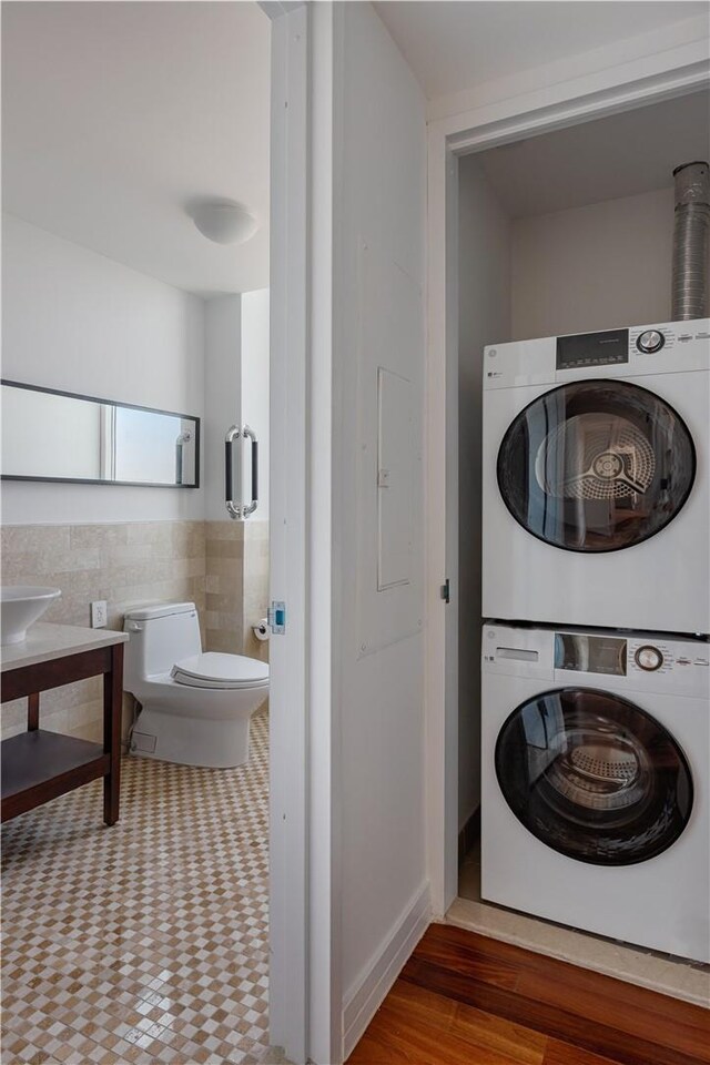 laundry area featuring tile patterned flooring, stacked washer / dryer, and tile walls