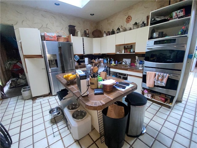 kitchen with sink, white cabinets, light tile patterned floors, and appliances with stainless steel finishes