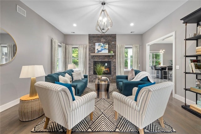 living room with a notable chandelier, a stone fireplace, and dark wood-type flooring