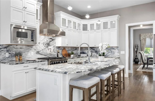 kitchen featuring light stone countertops, dark hardwood / wood-style flooring, stainless steel appliances, wall chimney range hood, and white cabinets