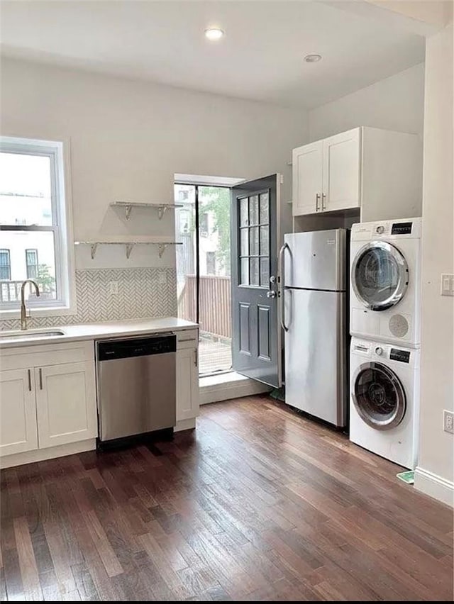 kitchen with sink, dark hardwood / wood-style floors, white cabinets, stacked washer and clothes dryer, and appliances with stainless steel finishes