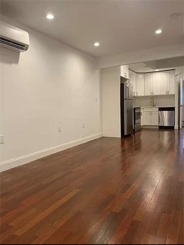 unfurnished living room featuring a wall mounted air conditioner, dark hardwood / wood-style floors, and sink