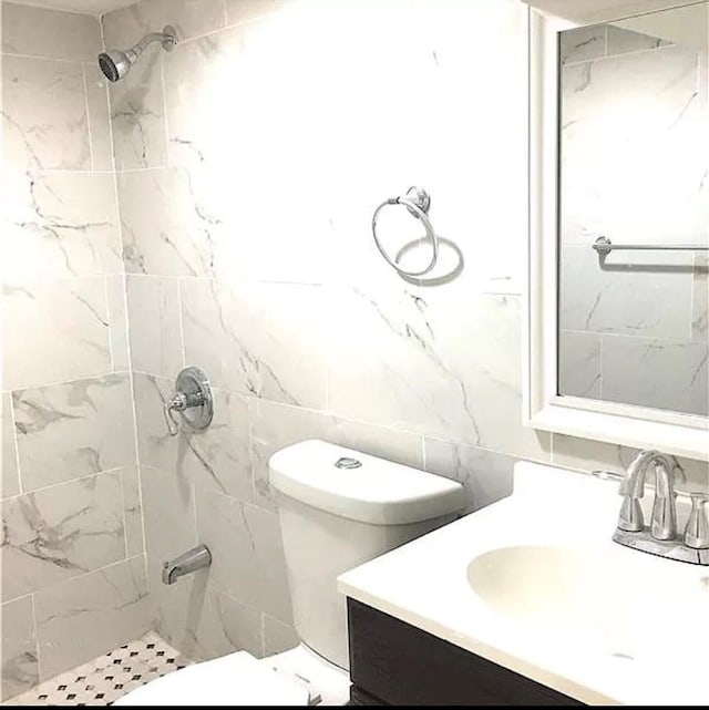 bathroom featuring toilet, vanity, tile walls, and tiled shower