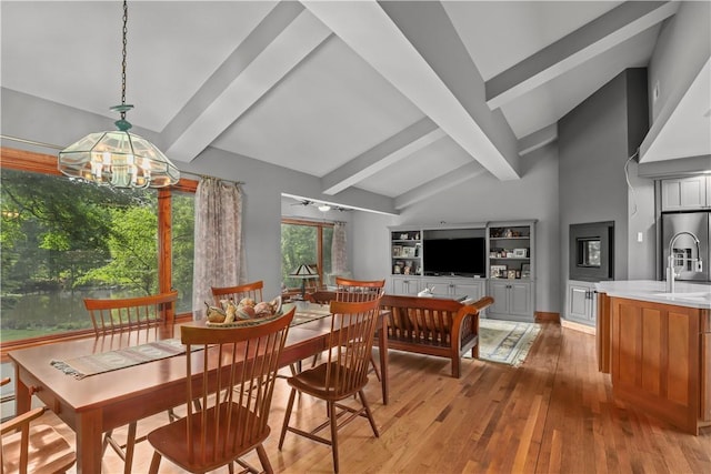 dining room with light wood-type flooring, lofted ceiling with beams, a chandelier, and sink